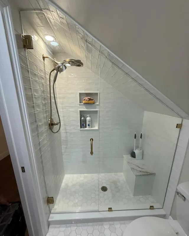 Frameless glass panel cut to fit a sloped ceiling over a tiled shower