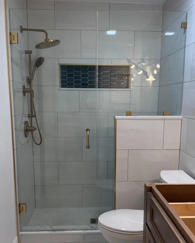 Frameless shower with brushed gold hardware and a tiled shampoo niche