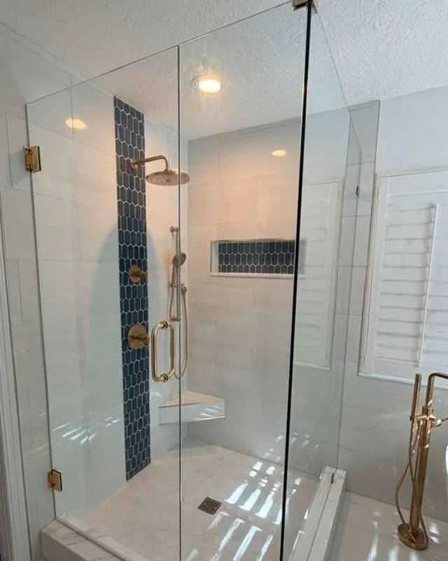 Frameless shower enclosure with gold hardware beside plantation shutters