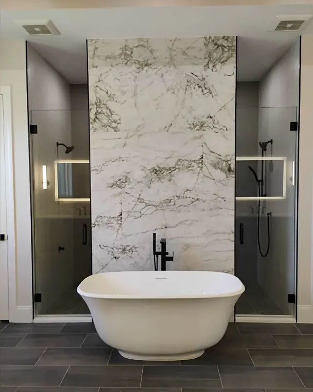 Freestanding tub beside a frameless glass shower panel with a marble slab wall
