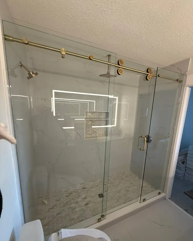 Frameless shower enclosure with brushed gold hardware and a lighted niche